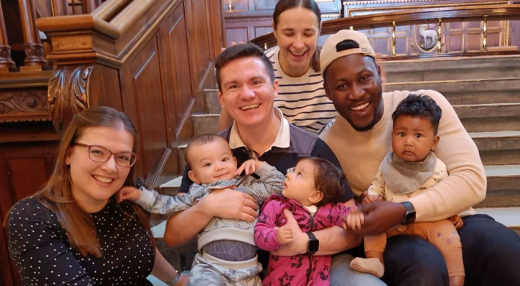 Four adults and three babies sit on the steps of Elias Church during a session of music and family time