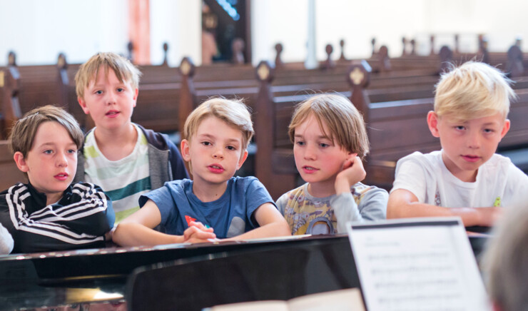 Børn samlet omkring et flygel i en kirke