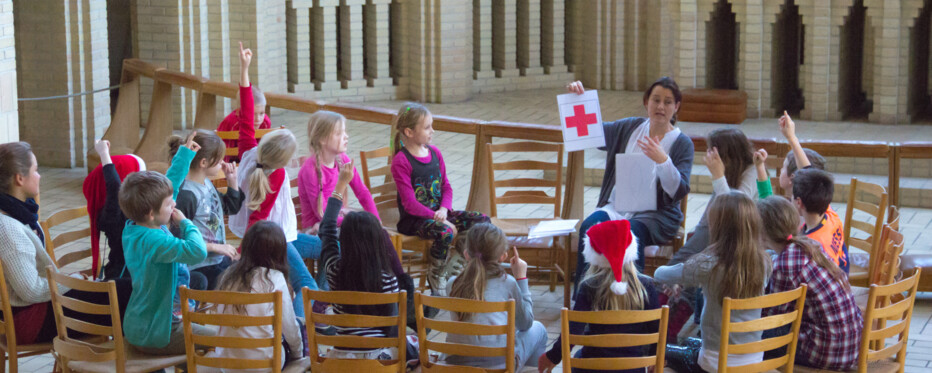 Børn sidder i en rundskreds i en kirke og lytter på en voksen