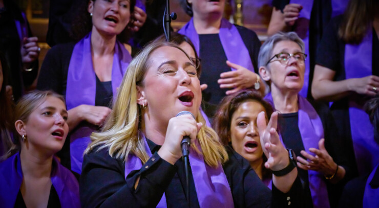 A gospel singer sings passionately in front of a large group of gospel singers