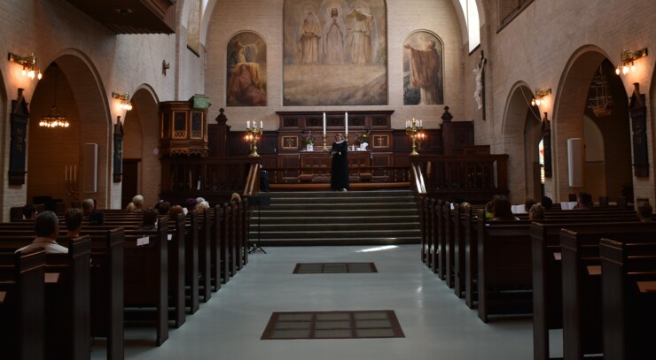 Inside the Elias Church during a Sunday Jazz Service. In front of the altar, Pastor Maria reads aloud from the Bible whilst church goers listen attentively